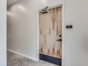 Una puerta con panel de madera, umbral negro y una pequeña placa con el número '1D'.