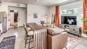A modern kitchen with a dining area, a television, and a large window with curtains. - Midtown OKC 1Bed Hideaway (Oklahoma City)