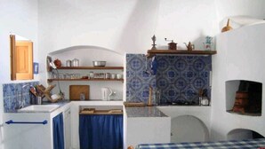Eine kleine Küche mit Spüle, Herd und Regalen, ein Essbereich mit kariertem Tisch und ein kleines Fenster.
