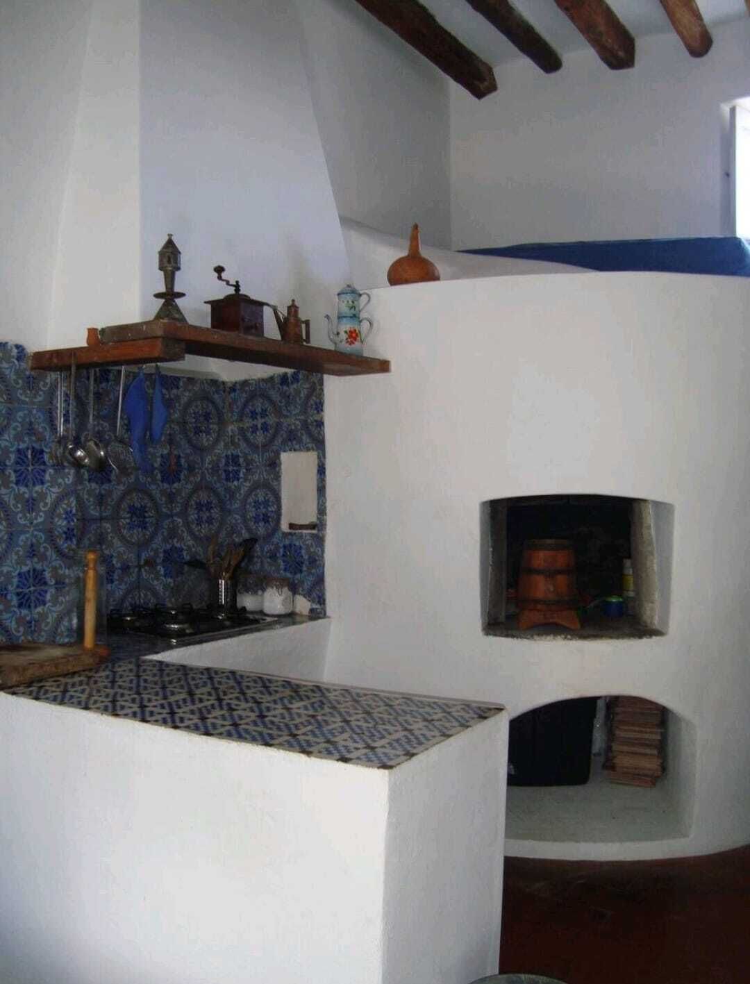 A kitchen with a blue patterned backsplash, a hanging pot rack, and a small oven built into the wall.