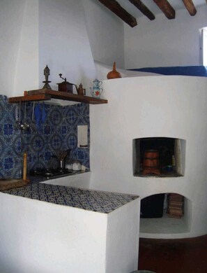 Eine KĂŒche mit blau gemustertem Fliesenspiegel, einer hĂ€ngenden Topfhalterung und einem kleinen, in die Wand eingelassenen Backofen.