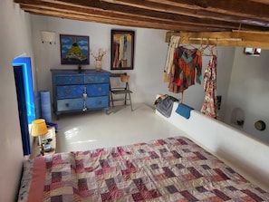 A bedroom with a bed, dresser, clothes rack, and artwork.