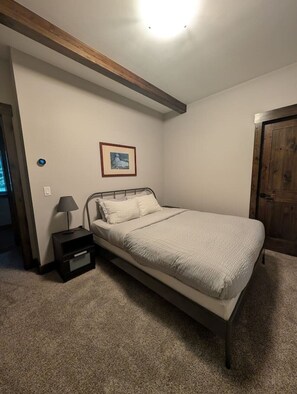 Ein Schlafzimmer mit einem Einzelbett, einem Nachttisch, einer Lampe, einem gerahmten Bild an der Wand und einer Holztür.