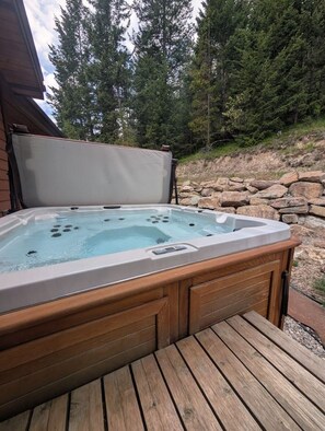Ein Whirlpool mit Holzaußenverkleidung, auf einer Holzdielen-Terrasse gelegen, umgeben von einer Steinmauer und Bäumen.