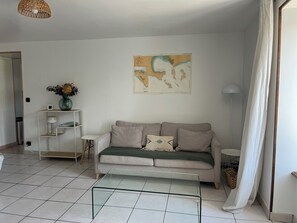 A living room with a sofa, a glass coffee table, a map on the wall, a small shelf with a vase, and a floor lamp. - House 6 persons / 2 bedrooms Ver sur mer (Ver-sur-Mer)