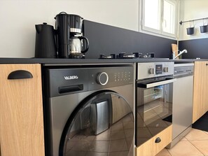 Eine kompakte Küche mit einer Frontlader-Waschmaschine, einer Kaffeemaschine und einem Geschirrspüler.