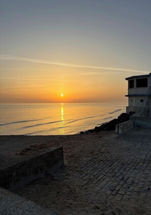 Un coucher de soleil sur une plage, avec un bâtiment sur la droite.