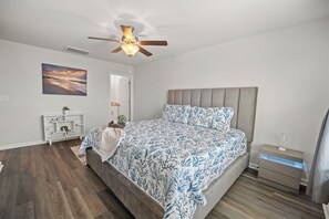 Ein Schlafzimmer mit einem Bett, einem Nachttisch, einem Deckenventilator, einem an der Wand befestigten Regal und einem Gemälde.