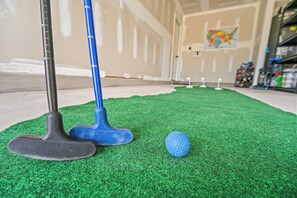 Minigolfbane med grøn græstørv, blå putter og en golfbold.