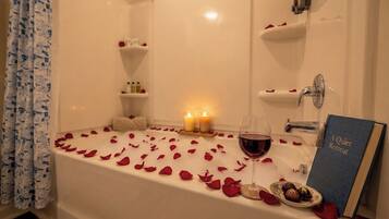 Eine Badewanne mit Rosenblättern, Kerzen und Pralinen.