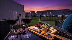 Une table avec des verres à vin, du fromage et des fruits sur un balcon offrant une vue sur les bâtiments au crépuscule.
