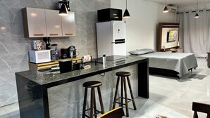 Una cocina moderna con encimera de mármol, microondas, refrigerador y cafetera. Hay dos taburetes en la barra.