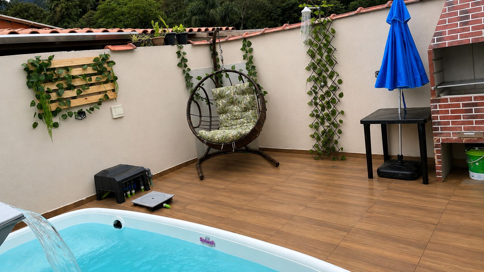 A swimming pool, a hanging chair, a brick oven, and a blue umbrella.