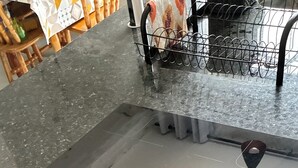 Una cocina con mostrador negro, un lavamanos y una estantería metálica.