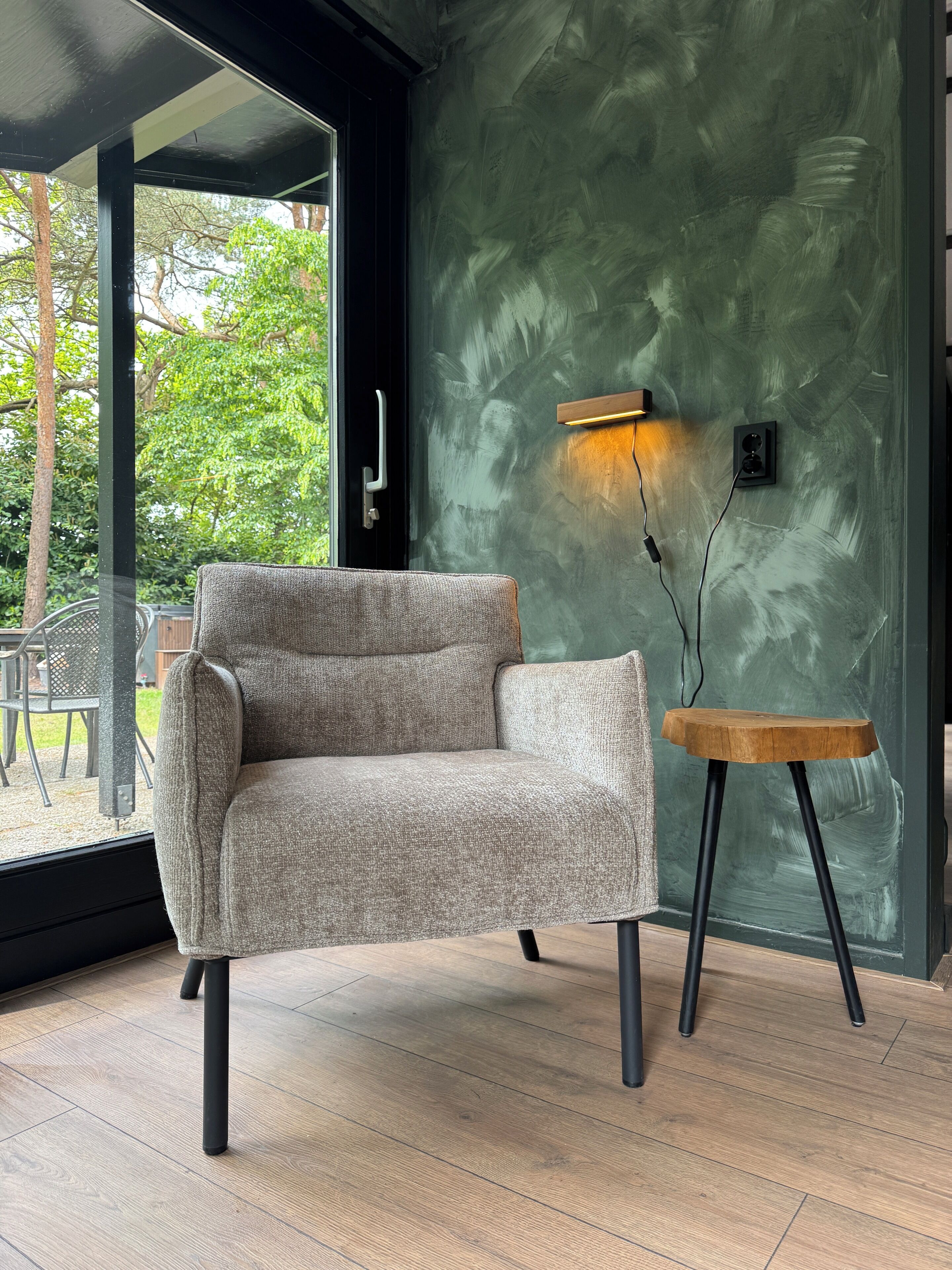 A modern living room with a grey sofa, a small wooden side table, and a green textured wall.