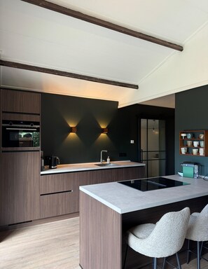 A modern kitchen with a built-in oven, a sink, and a dining area with chairs. - New: Luxury forest house in nature with private hot tub (Rheezerveen)