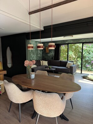 A modern dining area with a round table, six chairs, and hanging pendant lights. - New: Luxury forest house in nature with private hot tub (Rheezerveen)