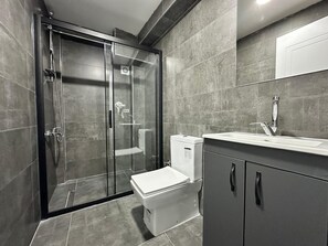 Un baño moderno con ducha envuelta en vidrio, inodoro y lavamanos con gabinete.