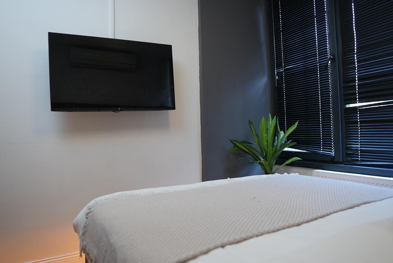Une chambre à coucher avec un lit, un téléviseur à écran plat fixé au mur et une fenêtre avec des stores.