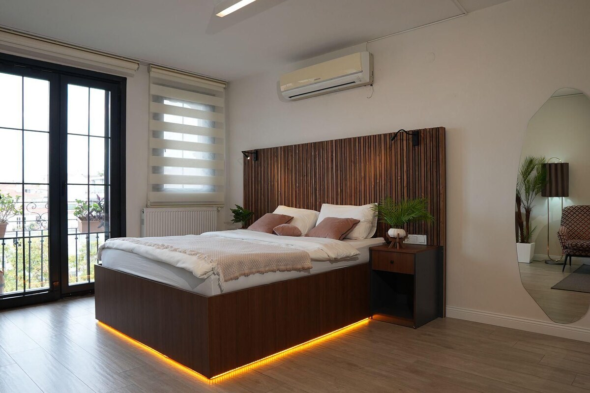 Un dormitorio moderno con un cabecero de madera, una mesita de noche con lámpara y vistas a través de un ventanal.