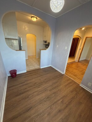 A hallway with wooden flooring, a red basket, and a kitchen area with cabinets and a countertop.