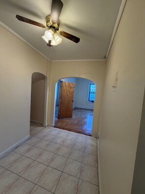 A hallway with a ceiling fan, a door leading to another room, and a tiled floor.