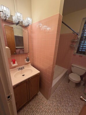Un bagno con piastrelle rosa, un lavandino, uno specchio, un water e una zona doccia.