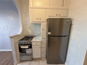 A compact kitchen with a gas stove, a stainless steel refrigerator, and white cabinetry.