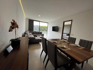 A modern dining area with a wooden table set for four, a sofa, and a large window. - New apartment in Ladrón de Guevara, centrally located—downtown area   (Guadalajara)