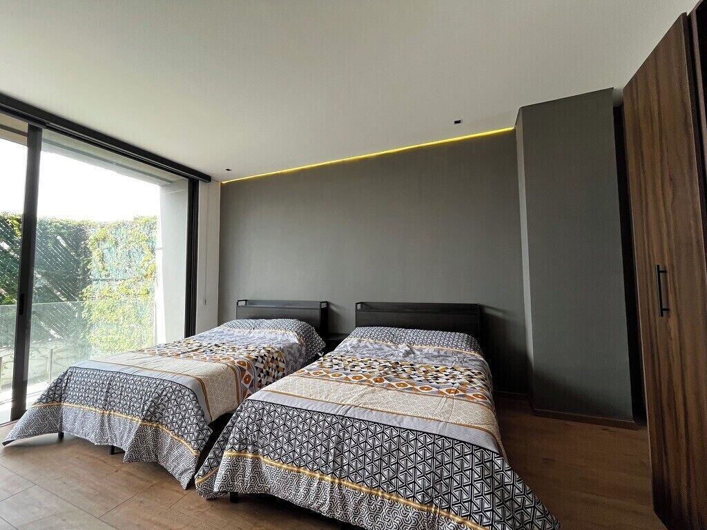 Een moderne slaapkamer met twee bedden, grote ramen en uitzicht op groen.