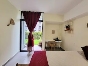 Une chambre avec un lit, un bureau et une chaise. Il y a une fenêtre avec des rideaux, une plante en pot et une étagère fixée au mur.
