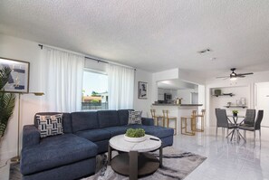 Ein modernes Wohnzimmer mit einem Ecksofa, einem runden Couchtisch und einem Essbereich mit Glastisch und Stühlen.