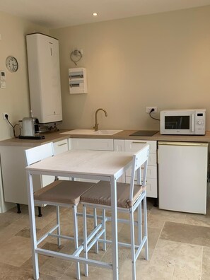 Une cuisine compacte avec une table blanche, un évier, un four à micro-ondes et un chauffe-eau.