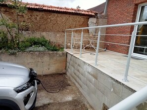 Une voiture blanche est garée dans un espace étroit, contre un mur en béton et une rambarde métallique.