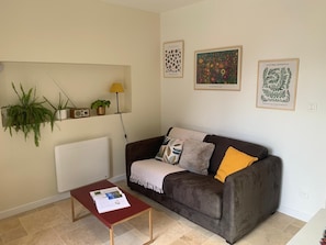 A living room with a brown sofa, a red coffee table with a magazine, a lamp, and wall-mounted plants.
