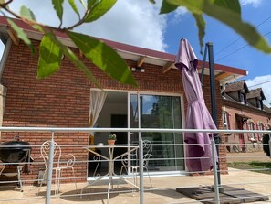 Une maison en briques avec une porte-fenêtre coulissante, un patio avec un barbecue et un parasol violet.