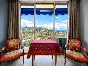 Ein Balkon mit Tisch und zwei Stühlen, Blick auf eine Stadt und ein blaues Markisenverdeck.