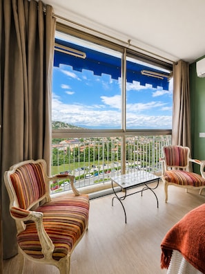 Un balcon avec vue sur le paysage urbain, deux fauteuils Ă rayures, une petite table et un plaid blanc.
