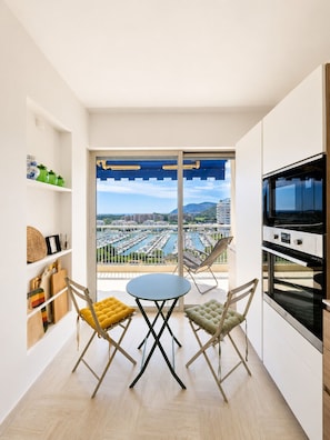 Un balcon donnant sur une marina et sur des immeubles, une table ronde, deux chaises et un coin cuisine avec un four.