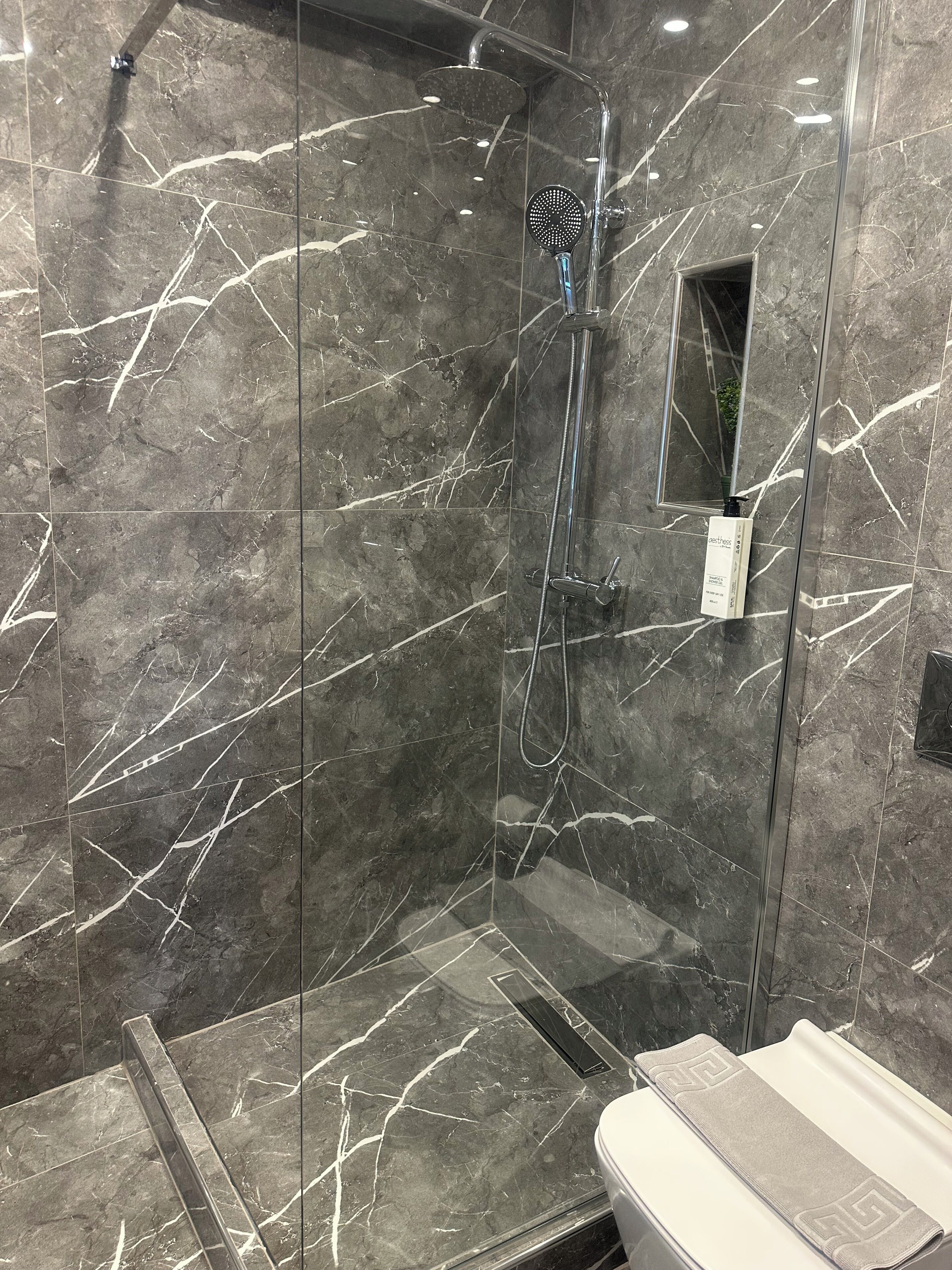 Une salle de bain moderne avec une douche en verre, des murs en marbre et un lavabo blanc.