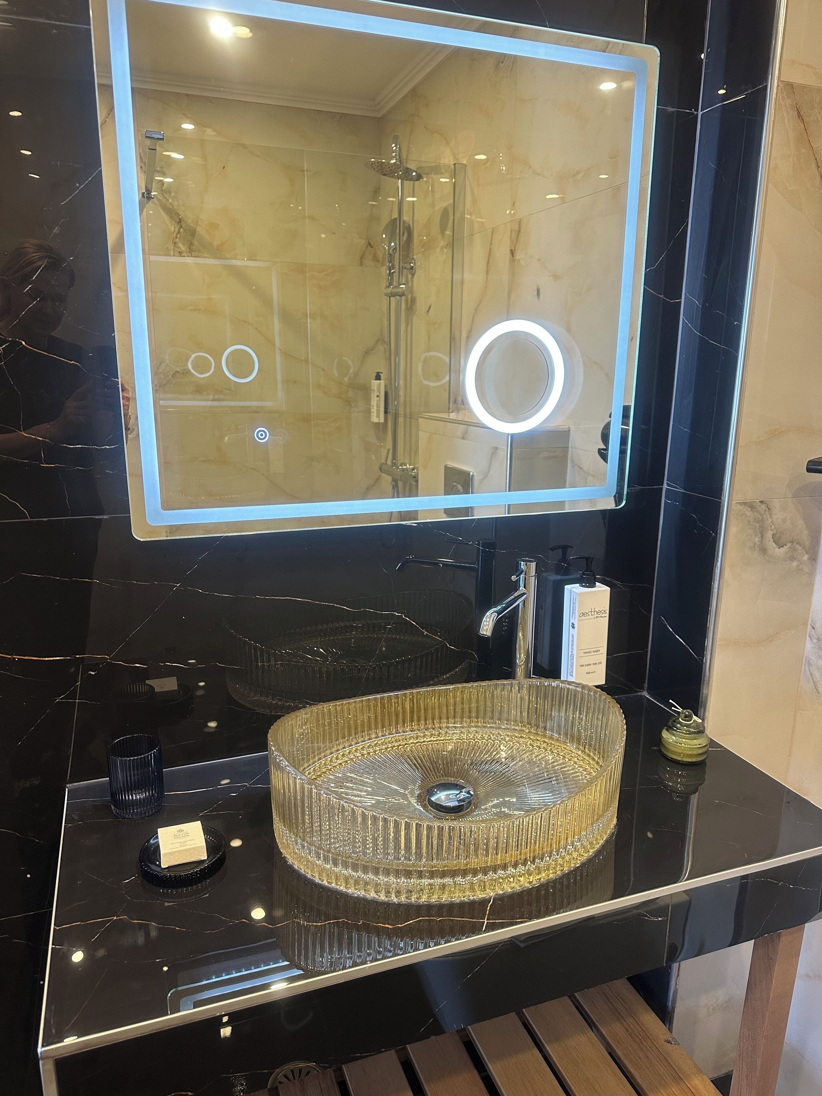 Un bagno con uno specchio grande, un lavabo con bordo dorato e un soffione a mano.