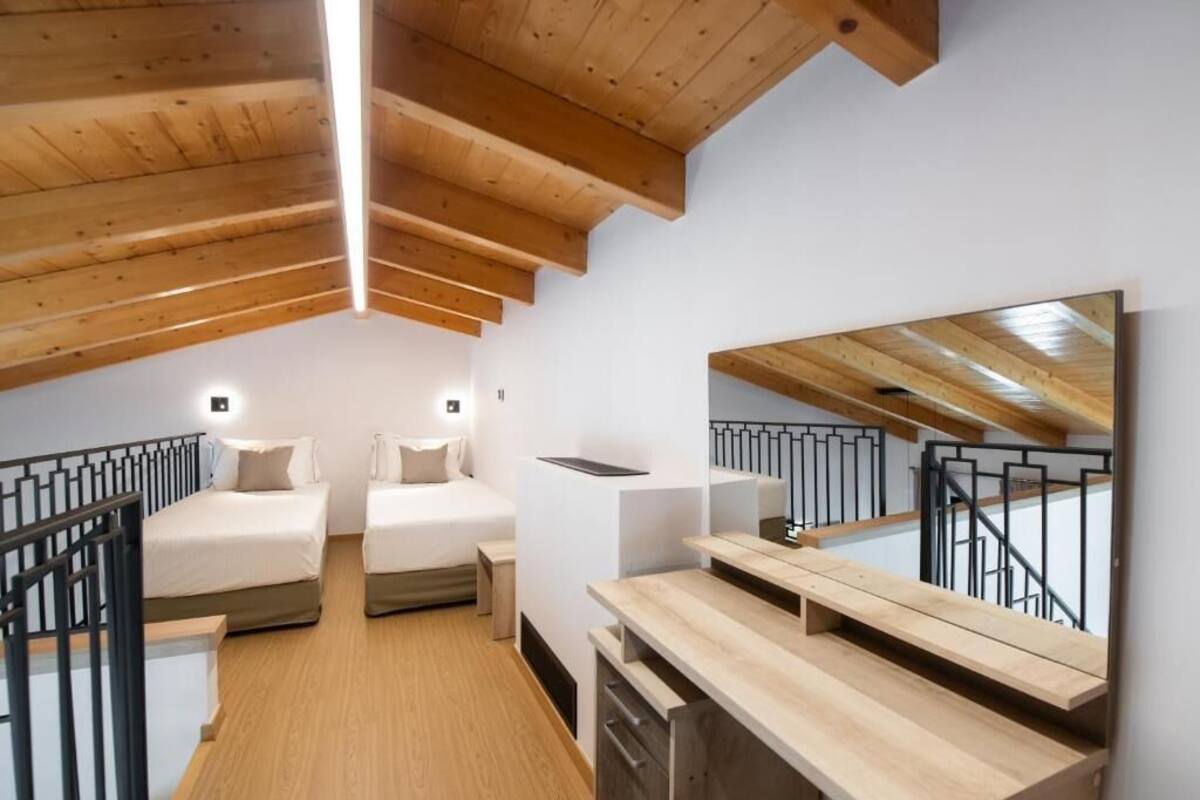 A loft bedroom with two beds, a wooden ceiling, a large mirror, and a wooden desk.