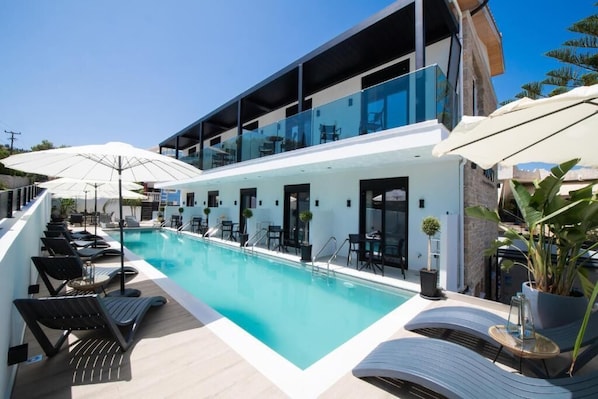 A modern hotel with a pool, outdoor seating, and a glass-enclosed upper level. - Solvio Boutique Hotel (Lefkada)