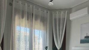 A modern living room with a sofa, a coffee table with a vase, sheer curtains, and a painting on the wall.