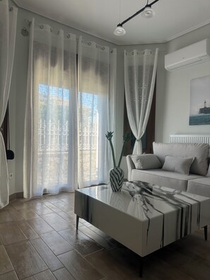 Una sala de estar moderna con un sofá, una mesa de centro con un jarrón, cortinas translúcidas y un cuadro en la pared.