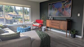 Un salon moderne avec un canapé, un pouf, un fauteuil rouge, un meuble en bois et un grand tableau abstrait.