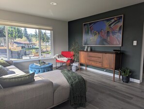 Ein modernes Wohnzimmer mit einer Couch, einem Hocker, einem roten Sessel, einer Holzkommode und einem großen abstrakten Gemälde.