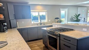 Une cuisine moderne avec des meubles de couleur sombre, un grand îlot central, une cuisinière à gaz et un four encastré.