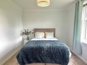 A bedroom with a bed, a nightstand, a vase with flowers, and a window with curtains. - Attractive colinton property for family (Edinburgh)