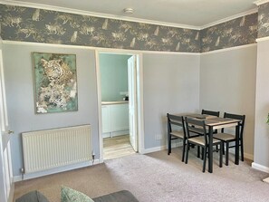 A room with a dining table and chairs, a radiator, a door leading to a kitchen, and a leopard print artwork on the wall. - Attractive colinton property for family (Edinburgh)